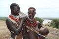 A young karo woman is painting the face of another woman carrying her child in her arms