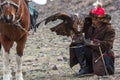 Young Kazakh Eagle Huntress Berkutchi woman with horse while hunting to the hare with a golden eagles on his arms Royalty Free Stock Photo