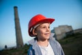 Young smiling kid with happy face wearing red orange helmet on factory industry plant with pipe background on dusk