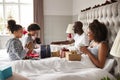 Young kids opening gifts on parentsÃ¯Â¿Â½ bed on Christmas morning while their parents sit up in bed watching, side view Royalty Free Stock Photo