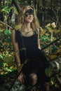 A young kind witch in a black dress with a black mask in a mystical forest in various poses. Art processing Royalty Free Stock Photo