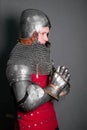A young knight in medieval armor prays with his hands clasped