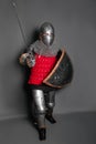 A young knight in medieval armor with a weapon in his hands kneeled