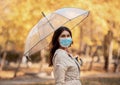 Young lady in antiviral mask walking with umbrella at autumn park on rainy day Royalty Free Stock Photo