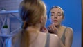 Young lady applying acne cream with cotton pad looking in mirror, facial hygiene