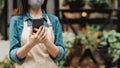 Young lady in apron and protective mask writes on phone and accepts online order at bouquet flower shop