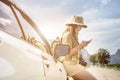 Young lady backpaker sitting on the car and using smart phone