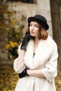 A young lady in a black hat and gloves and a light coat stands and looks outwardly. Retro. Outdoors.