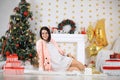 Happy young lady with curlu hair gifts by the fireplace near the Christmas tree. New year concept. Royalty Free Stock Photo