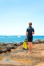 Young lady in diving suit with paddles standing on rock coast.