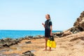 Young lady in diving suit with paddles standing on rock coast.