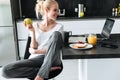 Young lady eating apple and using laptop in kitchen Royalty Free Stock Photo