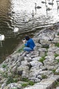 Young lady feeding swans on a river bank.