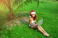 Young lady freelancer sitting on the grass with laptop in christmas hat in jungle Royalty Free Stock Photo
