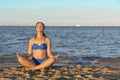 Young lady practicing yoga. Beautiful woman posing at sand beach. Workout near ocean sea coast. Fitness model caucasian ethnicity Royalty Free Stock Photo