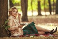 Young lady in retro style, student in park in nature wearing glasses and holding notepad in her hands