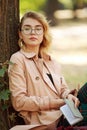 Young lady in retro style, student in park in nature wearing glasses and holding notepad in her hands