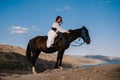 A young lady rider in a white dress is sitting in the saddle on a horse hugging her, against a beautiful mountain Royalty Free Stock Photo
