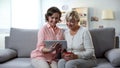 Young lady showing mother cute photos on tablet, spending time together, fun