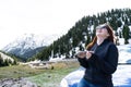 young lady sitting on a bonnet of a car using smart phone in the mountains. Happy Girl sending message with sun glasses Royalty Free Stock Photo