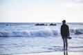 Young lady standing on the coast of the ocean crashed by foamy waves