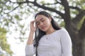 A young lady standing outside the park closes her eyes and touches the temple of her head as she experiences headache