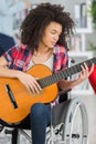 young lady in wheelchair at home playing guitar Royalty Free Stock Photo