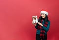 Young lady wiht santa hat and holding Christmas gift isolated red background. Emotion smile. Event x-mas valantine