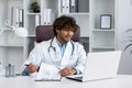 A young Latin American doctor consults patients online. He sits in the office in front of a laptop and talks through a Royalty Free Stock Photo