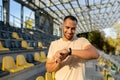 Young Latin American male sportsman stands at the stadium and looks at the fitness bracelet, the watch on his hand