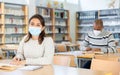 Young latin american woman in protective mask studying in library Royalty Free Stock Photo