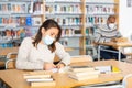 Young latin american woman in protective mask studying in library Royalty Free Stock Photo