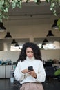 Young latin business woman using mobile phone standing in office, vertical. Royalty Free Stock Photo