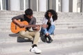 A young latin couple in love playing the guitar and singing sitting on stairs