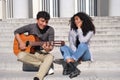 A young latin couple in love playing the guitar and singing sitting on stairs