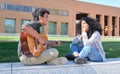 Young latin couple in love playing the guitar and singing at the university campus