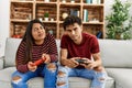 Young latin couple unhappy playing video game sitting on the sofa at home Royalty Free Stock Photo