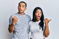 Young latin couple wearing casual clothes surprised pointing with hand finger to the side, open mouth amazed expression Royalty Free Stock Photo