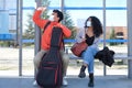 Young latin couple wearing protective face mask and carrying guitar case looking at the bus, sitting at bus stop