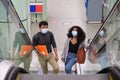 Young latin couple wearing protective face mask walking up into the escalators at the train or metro station