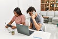 Young latin couple working using laptop and talking on the smartphone sitting on the table at home Royalty Free Stock Photo