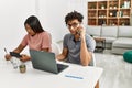 Young latin couple working using laptop and talking on the smartphone sitting on the table at home Royalty Free Stock Photo