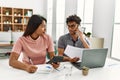 Young latin couple working using laptop and talking on the smartphone sitting on the table at home Royalty Free Stock Photo