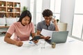 Young latin couple working using laptop and talking on the smartphone sitting on the table at home Royalty Free Stock Photo