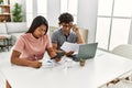 Young latin couple working using laptop and talking on the smartphone sitting on the table at home Royalty Free Stock Photo