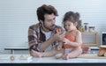 Young Latin father and little daughter cooking in the kitchen at home. Dad is feeding a cookie they made together to lovely gir