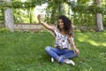 Young latin girl with dark skin and long curly hair taking a selfie with her smartphone sitting in a park Royalty Free Stock Photo