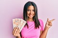Young latin girl holding 10 united kingdom pounds banknotes smiling happy pointing with hand and finger to the side