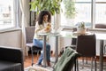 Young latin girl sitting at cozy home holding mobile phone using laptop. Royalty Free Stock Photo