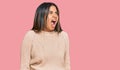 Young latin girl wearing wool winter sweater angry and mad screaming frustrated and furious, shouting with anger Royalty Free Stock Photo